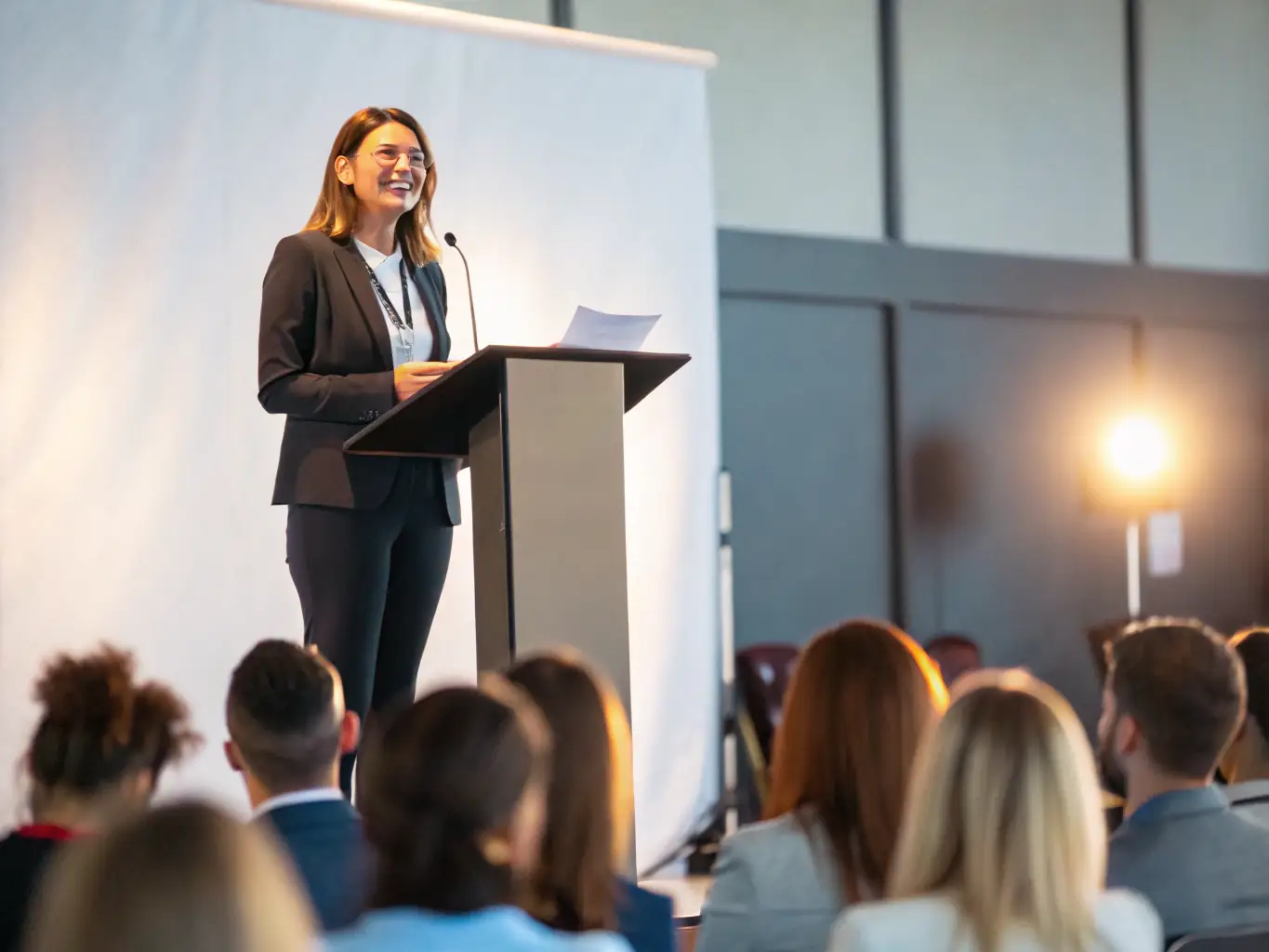 A professional headshot of a confident woman, Dr. Anya Sharma, in business attire, smiling warmly. The background is a blurred image of a conference stage.